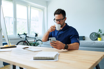 Man working from home office browsing phone and drinking coffee