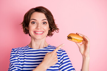 Portrait of young ecstatic attractive cheerful smiling girl pointing finger at cheeseburger isolated on pink color background