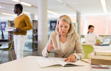 Woman with books sits at table in the library. High quality photo