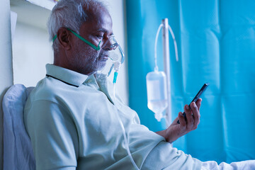 Sick elderly man with on ventilator Oxygen mask checking health status report on mobile phone -...