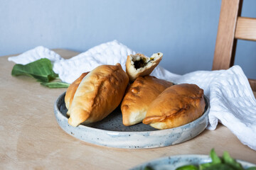 Pies stuffed with sorrel on a blue plate on a wooden table. Side view.