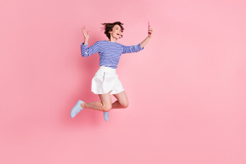 Full size photo of young beautiful excited happy cheerful girl take selfie say hi jump isolated on pink color background