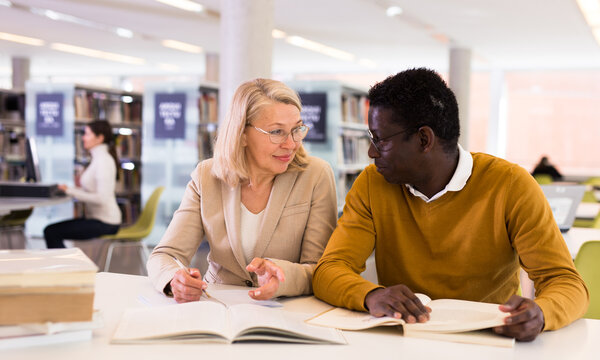 Friendly adult students preparing in library. High quality photo