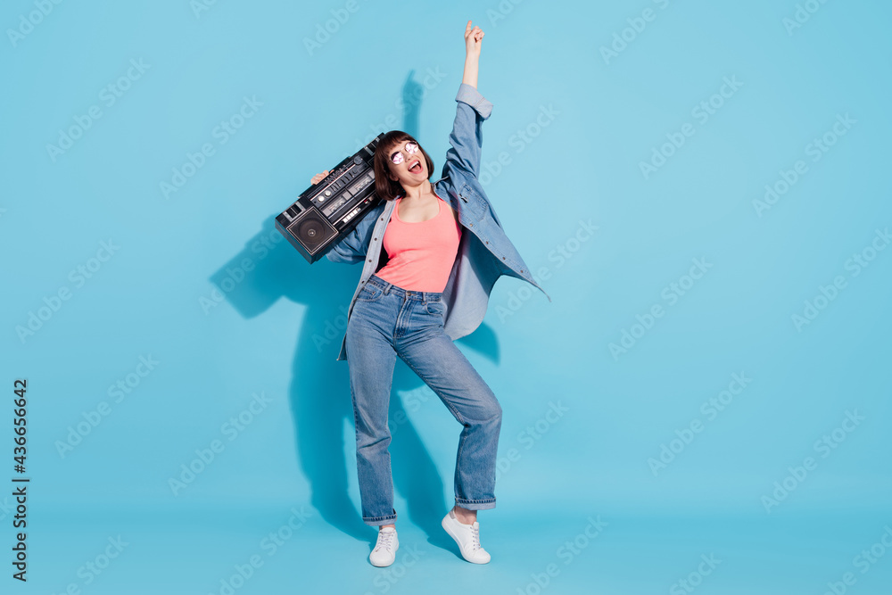 Wall mural Full size photo of crazy young lady dance with boom box wear top jeans eyewear isolated on blue color background