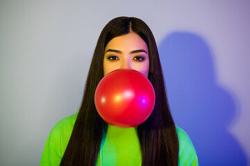 Photo of funny shiny young woman dressed green hoodie blowing red balloon isolated neon color background