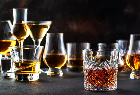 Hard strong alcoholic drinks, spirits and distillates in glasses in assortment: vodka, cognac, scotch, whiskey etc. Brown bar counter background