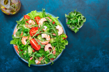 Shrimp salad with tomatoes, lettuce, arugula, avocado, cucumber and lemon dressing on blue table. Healthy eating, clean food concept. Top view