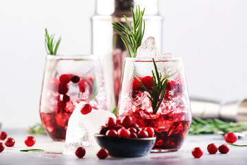 Cranberry, vodka, gin alcoholic cocktail with ice, rosemary and berries in tumbler glass. Summer long drink. Gray table background