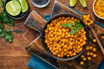 Fried chickpeas with turmeric in ceramic plate on an old wooden table background. Roasted spicy chickpeas or Indian chana or chole, popular snack recipe. Top view.
