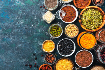 Various organic superfoods, beans, grains, cereals, legumes, seeds in reusable cans and jars. Copy space top view. Blue background