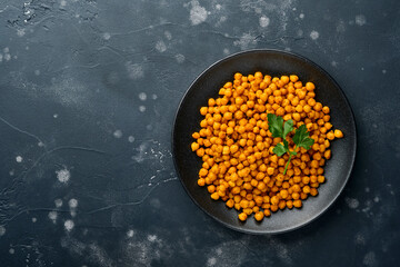 Fried chickpeas with turmeric with parsley and lime in black plate on an old black table background. Roasted spicy chickpeas or Indian chana or chole, popular snack recipe. Top view.