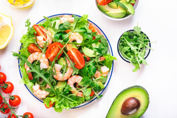 Summer shrimp salad with tomatoes, lettuce, arugula, avocado, cucumber and lemon dressing on white background. Healthy eating, clean food