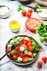Summer caprese salad with red tomatoes and white mozzarella cheese with fresh green basil leaves. Gray table. Top view