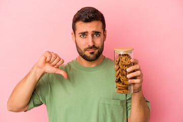 Young caucasian man holding cookies jar isolated on pink background showing a dislike gesture, thumbs down. Disagreement concept.