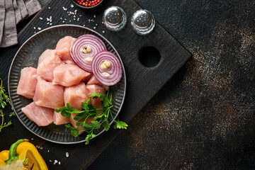 Raw pieces meat ingredients of chicken on wooden board, spices, herbs and vegetables on dark grey...