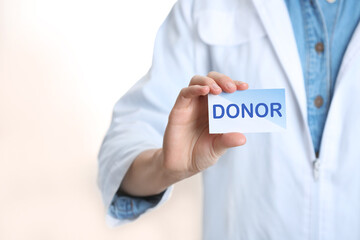 Doctor holding card with word DONOR on white background, closeup