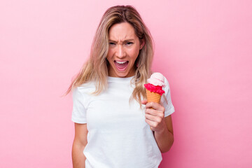 Young australian woman holding an ice cream isolated on pink background screaming very angry and aggressive.