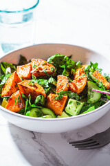 Baked sweet potato with green salad in a white bowl. Vegan food concept.