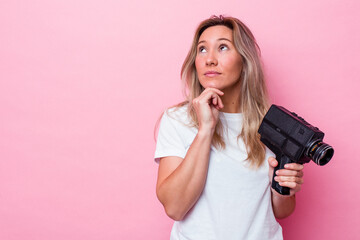 Young australian woman filming with a vintage video camera isolated looking sideways with doubtful...