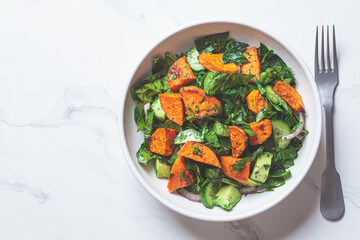 Baked sweet potato with green salad in a white bowl. Vegan food concept.