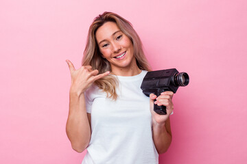 Young australian woman filming with a vintage video camera isolated showing a mobile phone call...