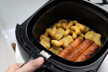 homemade nuggets and sausage are cooked by using a black air fryer or oil free fryer appliance for being lunch in afternoon