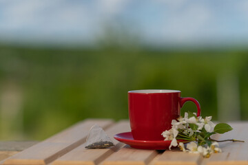 a disposable tea bag next to a red mug and a blossoming apple tree branch on a wooden table