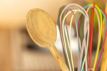 Close-up of wooden cooking spoon with colorful whisks in kitchen