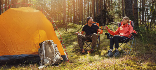 forest camping - young hiker couple enjoying cup of tee at campsite - obrazy, fototapety, plakaty