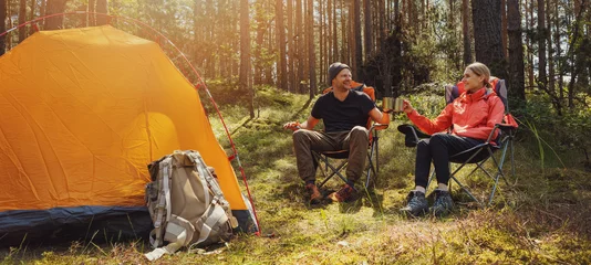 Wall murals Camping forest camping - young hiker couple enjoying cup of tee at campsite