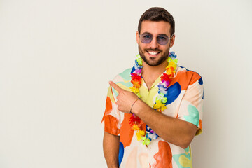Young caucasian man dancing on a hawaiian party isolated on white background smiling and pointing aside, showing something at blank space. - obrazy, fototapety, plakaty