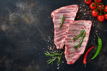 Raw pork ribs or fresh uncooked meat with spices on black wooden tray with paprika, garlic cloves...