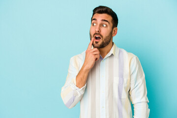 Young caucasian man isolated on blue background looking sideways with doubtful and skeptical expression.