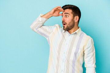 Young caucasian man isolated on blue background looking far away keeping hand on forehead.