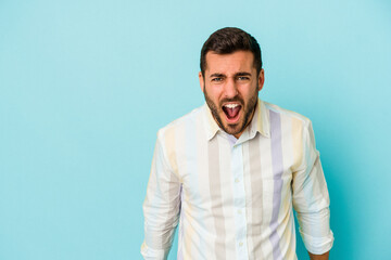 Obraz premium Young caucasian man isolated on blue background shouting very angry, rage concept, frustrated.