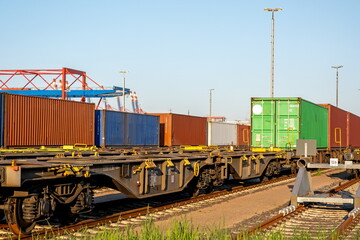 Railway freight waggons with containers on tracks in the harbour on a sunny day with blue sky and container bridges in the background