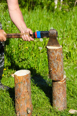 Lumberjack. A man chopping wood with an old metal axe, hatchet with a wooden handle in nature. Stumps of pine trees on green grass. Rural life, a household. Making a fire.