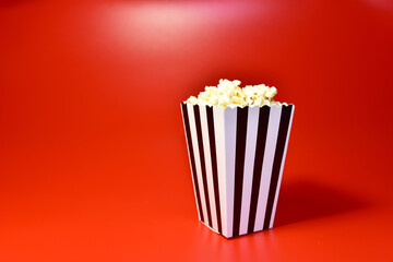 Popcorn in colored cardboard packaging. Heap of salted popcorn in paper striped bucketon a red background.