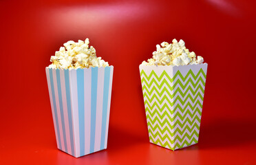 Popcorn in colored cardboard packaging. Heap of salted popcorn in paper striped bucketon a red background.