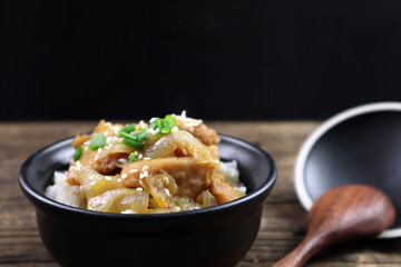 rice stir korean sauce with chicken in black ceramic bowl is served on the wooden table runner with wooden spoon with black wall background during dinner in the Japanese restaurant