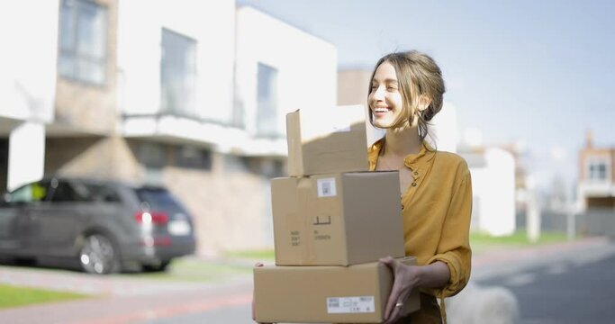 Young happy woman carries home a parcels with goods purchased online at the modern residential district. Concept of online shopping and delivery