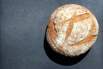 Round sourdough bread in the sunlight on a dark metallic surface. Copy space for text.