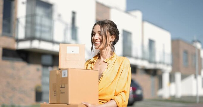 Young happy woman carries home a parcels with goods purchased online at the modern residential district. Concept of online shopping and delivery