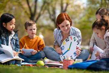 Teacher with small children sitting outdoors in city park, learning group education concept.