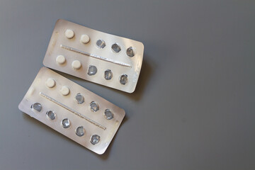 White tablets in a foil blister on a gray background, several tablets eaten. Copy space
