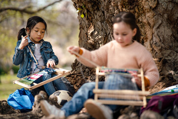 Small children with hand loom sitting outdoors in city park, learning group education concept.