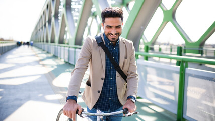 Young business man commuter with bicycle going to work outdoors in city, walking on bridge.