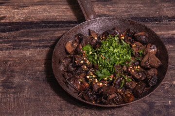 Fried royal champignons in an old cast-iron skillet with trendy hard light, dark shadow