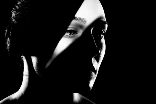 studio portrait of a beautiful young woman with shadows on her face, against dark backgroung. Black and white photo.