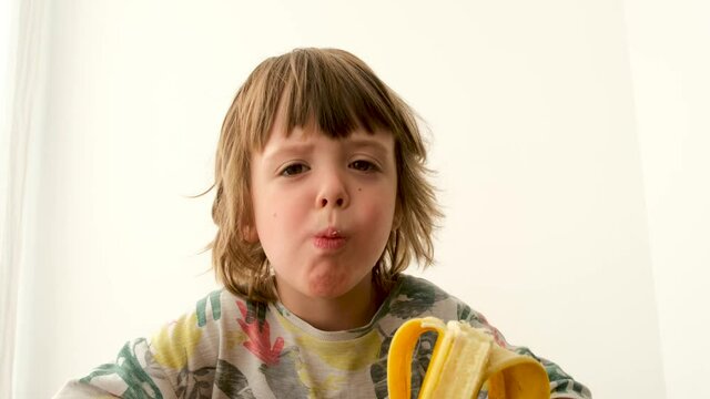 Cute boy of four years old eating a banana while at home on a white background